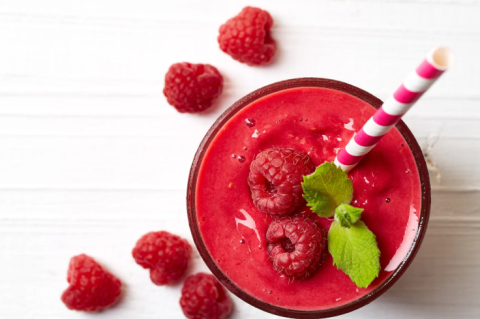Overhead view of a raspberry red shake with a straw and raspberries around it
