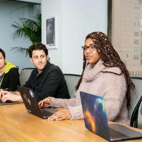 group of students sitting around a conference table with laptops