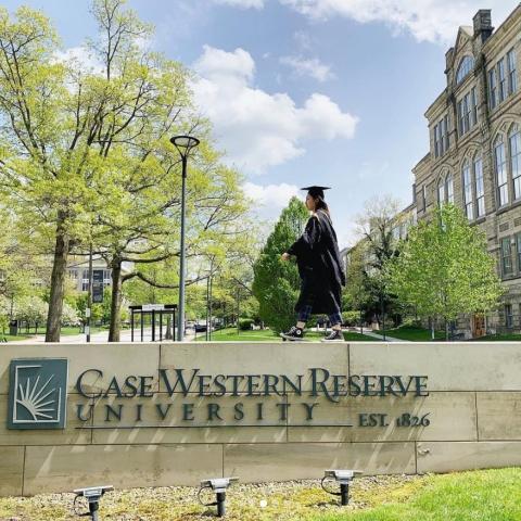 Student in graduation dress walking on CWRU signage