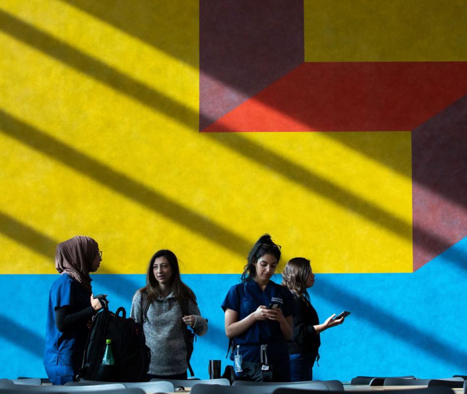 Five students talking to each other in front of a colorful mural