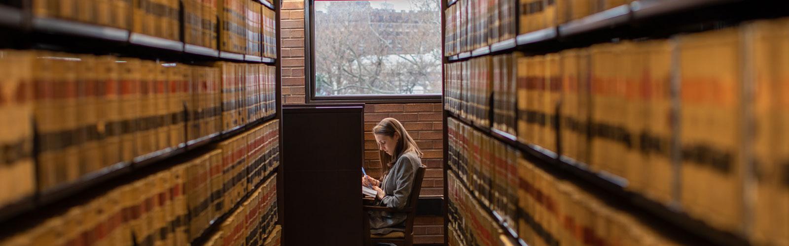 A CWRU law student sitting among the stacks of law journals in CWRU law library