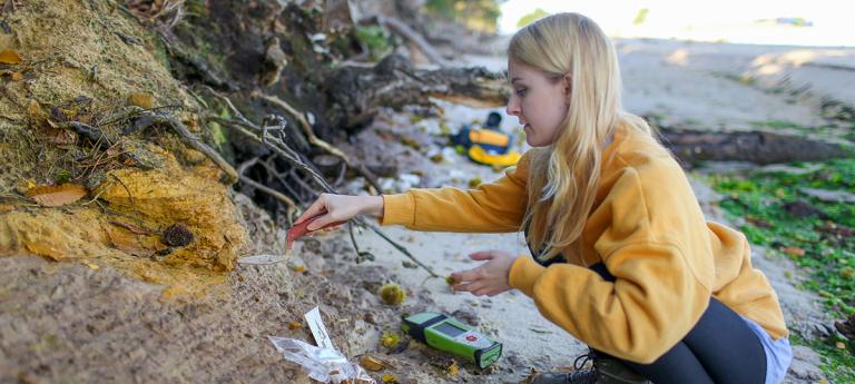 Final year female Geology student taking coastal rock samples