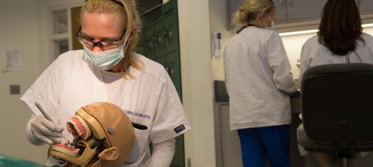 A woman practices dentistry on a dummy patient