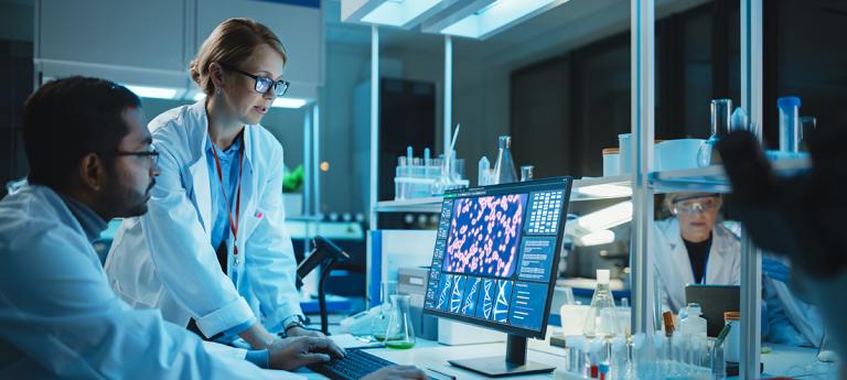 Female Research Scientist with Bioengineer Working on a Personal Computer with Screen Showing DNA Analysis Software User Interface. Scientists Developing Vaccine, Drugs and Antibiotics in Laboratory