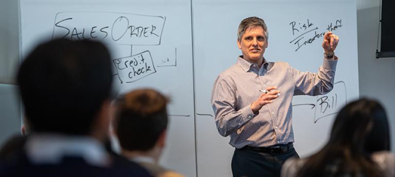 A man teaching finance up by a whiteboard