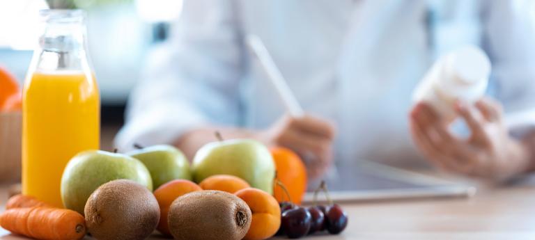 Woman nutritionist doctor writes the medical prescription for a correct diet on a desk with fruits, pills and supplements.