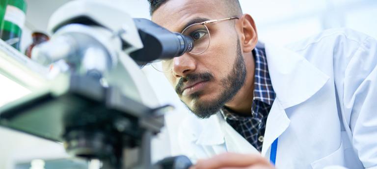 Portrait of young Middle-Eastern scientist looking in microscope while working on medical research in science laboratory