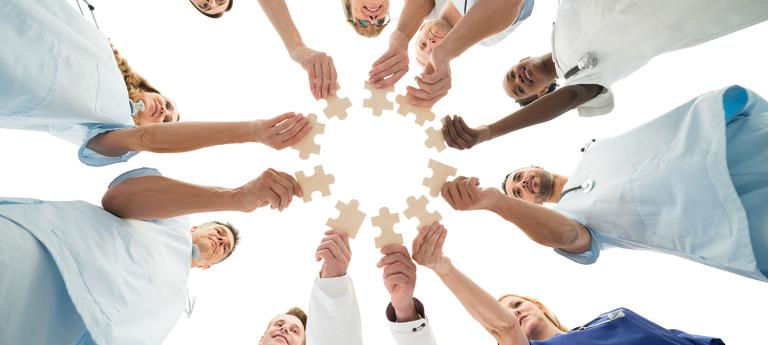 medical professionals standing in a circle holding puzzle pieces
