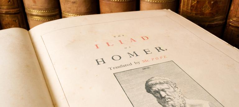 Close up of and Antique copy of the Iliad by Homer with leather bound books in the backgroun