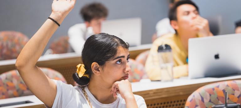 A student in a full lecture hall raises their hand