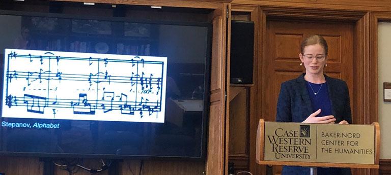 Case Western Reserve University faculty member standing at a podium next to a screen displaying sheet music