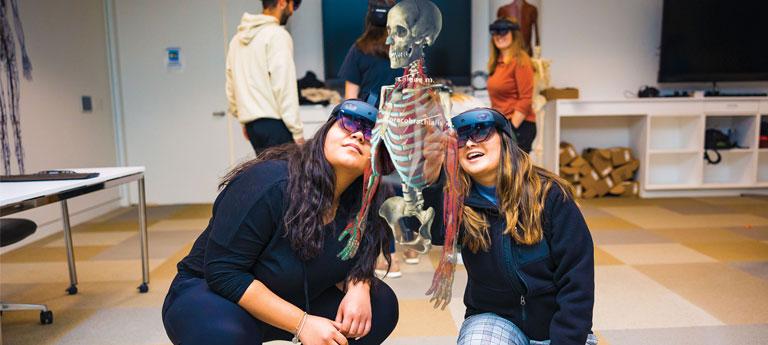 Two Case Western Reserve University dental students wear HoloLens headseats and point at a hologram body