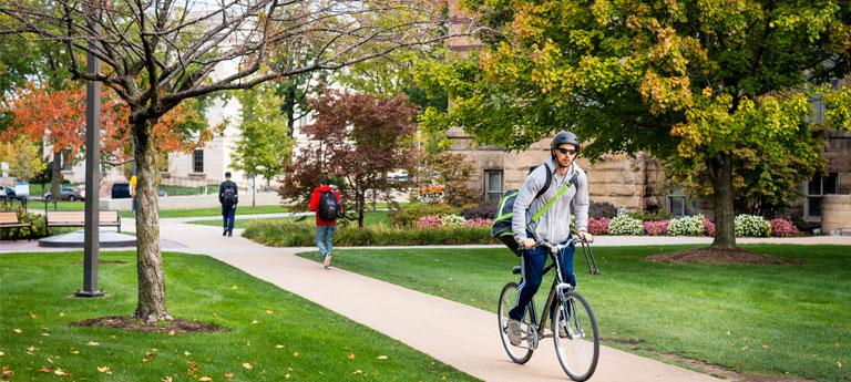 A Case Western Reserve University student biking on the Case Quad sidewalk