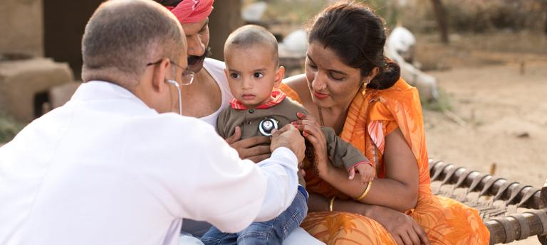 Back of a doctor talking to a child patient whose mother holds them
