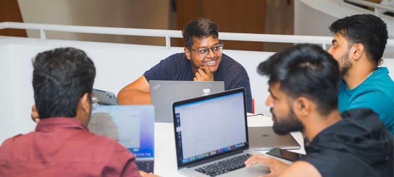 Four students sit at a round table talking inside Peter B. Lewis building at Case Western Reserve University