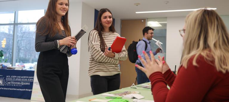 Two prospective students speak to a recruiter sitting at a table at the Mandel Placement Fair