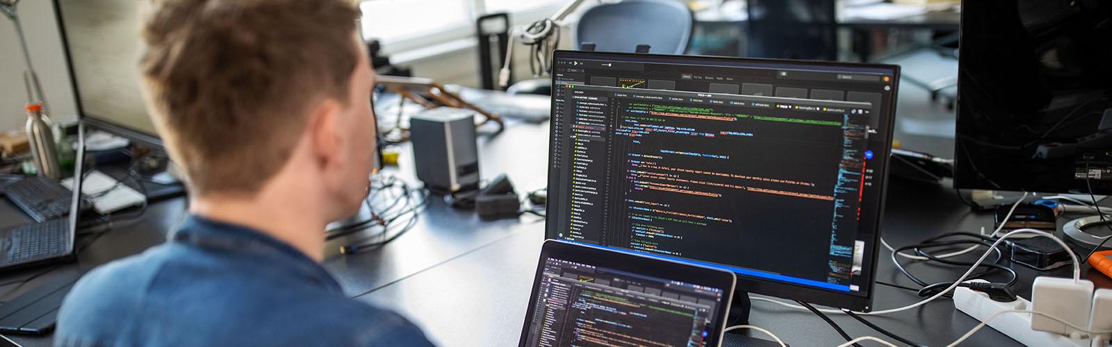 Student writing code on two computer screens