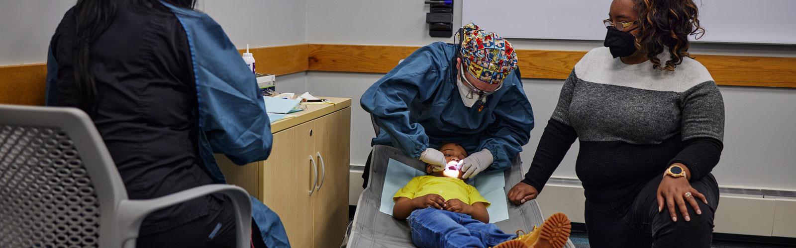 A Case Western Reserve University dental student provides care to a young patient with two other adults in the room