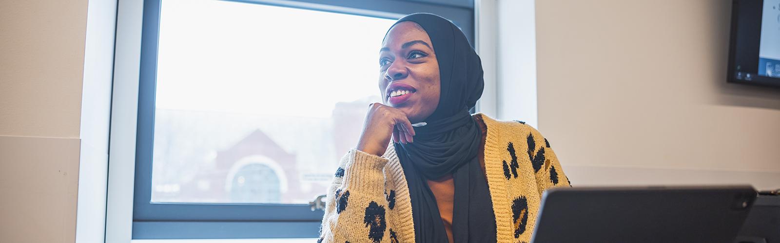 A Mandel student sits at a desk in front of a window smiling