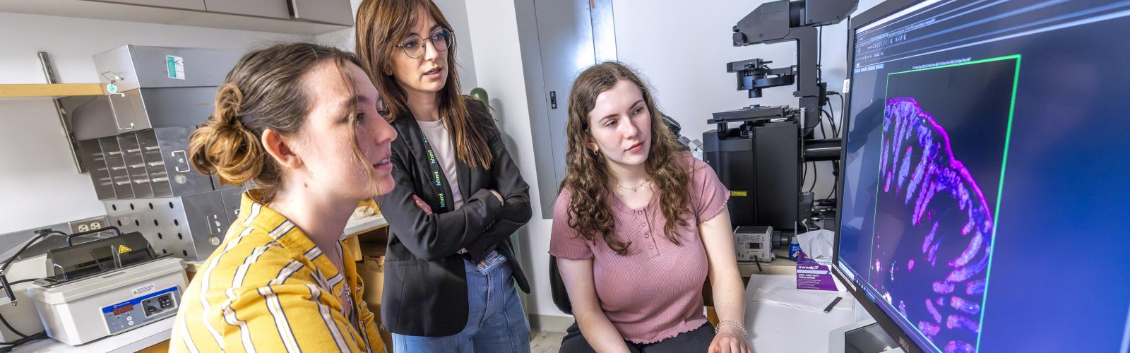 Two genomics students and a faculty member look at a computer screen