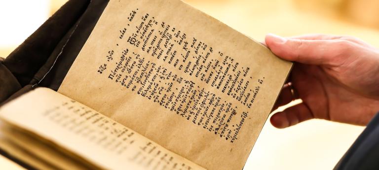 Close up of hands holding an ancient book with ancient Greek and in Old Slavonic text