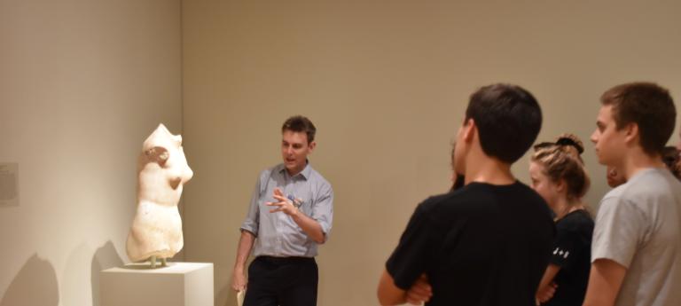 Students observe a professor talk about a classical marble statue at the Cleveland Art Museum