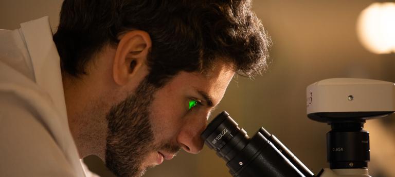 A close up side profile view of a Scientist looking into a Microscope