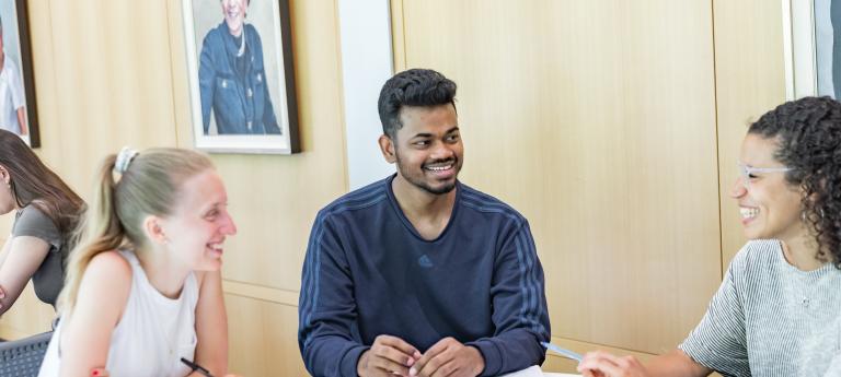 Three MSW students of various genders, ages and ethnicities chat at a table