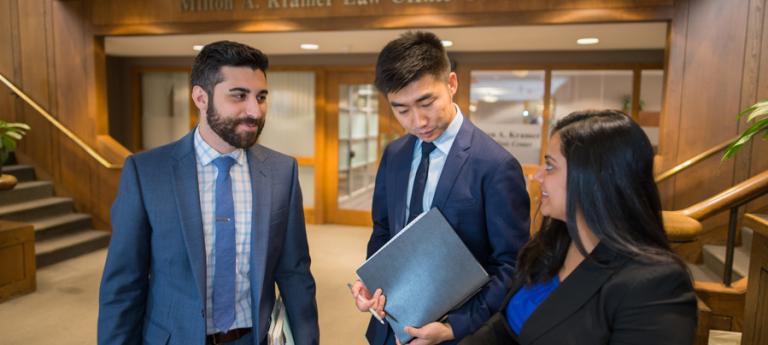 Three law students standing in front of the Kramer Law doors looking at a book