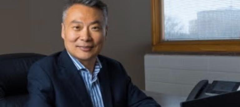 man with blazer and blue shirt seated in front of computer