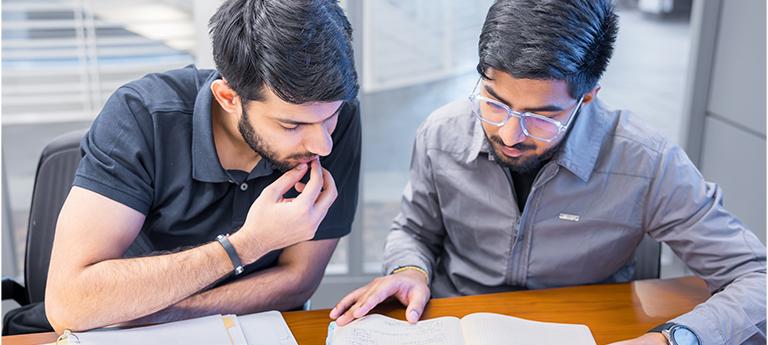 Two male students studying paper on table.
