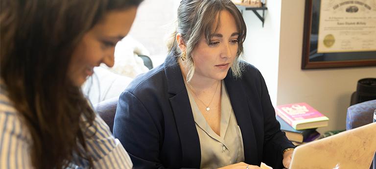 Two women working intently on a laptop in an office setting.