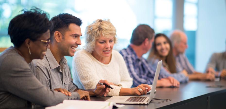 A group of faculty sitting at a table looking at a computer screen
