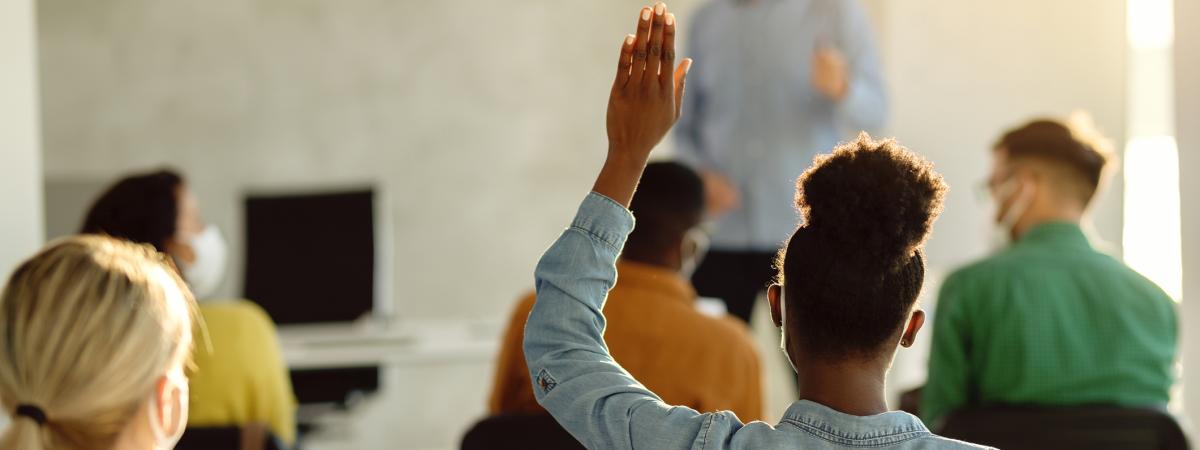 Girl with raised hand in a classroom with a professor wearing a mask