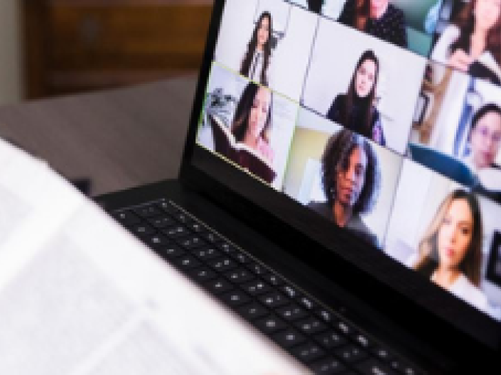 A laptop screen sharing people on a Zoom meeting and an open book.