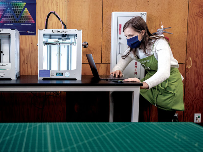 A person using a laptop next to a 3D printer.