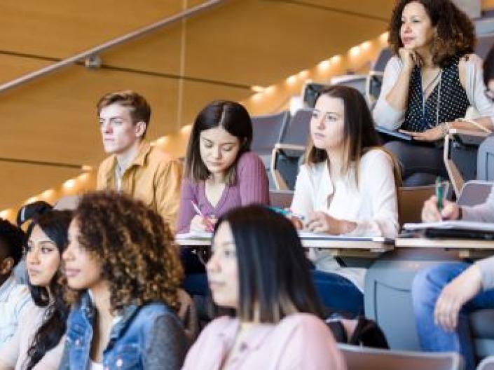 Students sitting in a classroom, one taking notes.