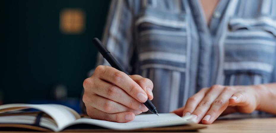 Close up of a woman sitting at a wooden table and taking notes while working from an office. 