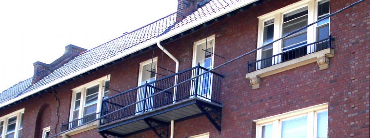 Upper story of long brick apartment building, with rail balcony and white windows