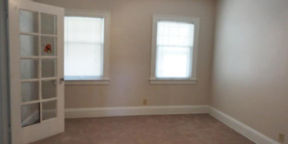 Creme colored bedroom with beige carpet and two large bright windows