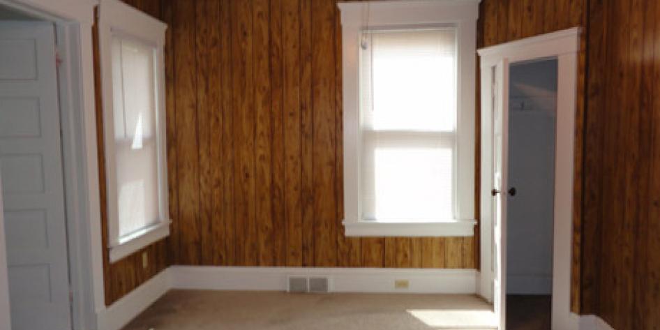 Brown, wood paneled wall bedroom with two bright windows and beige carpet
