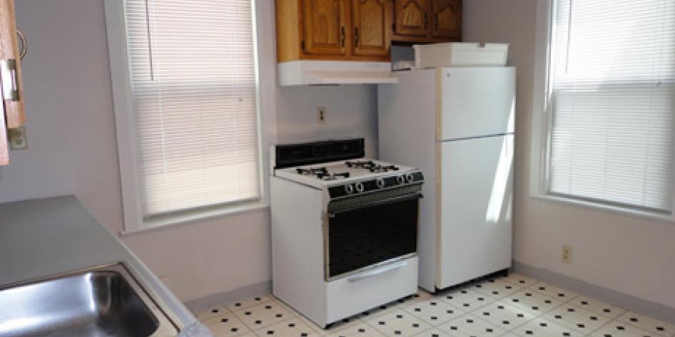 White kitchen with wood cabinets, refrigerator, stove and steel sink, with two bright windows