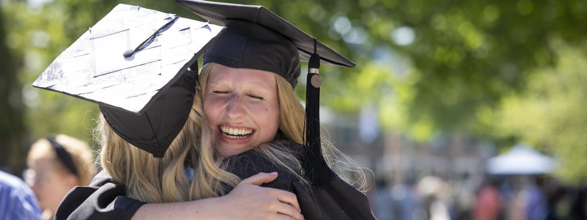 Two students in caps and gowns hugging.