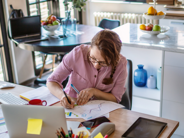 A women works on slides for a presentation in front of a laptop while sitting in a kitchen