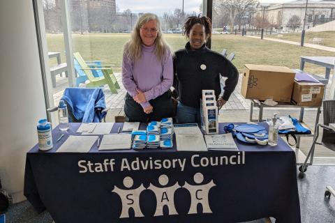 Two women stand behind a Staff Advisory Council table at Employee Appreciation Day 2024