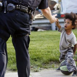 Photograph of a young African American boy reaching his hand out towards a uniformed white police officer