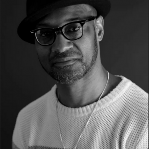 Photograph of Daniel Gray Kontar, a Black man wearing glasses and a hat, looking into the camera
