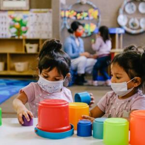 Photograph of two young children wearing COVID masks and playing with blocks in a day care center