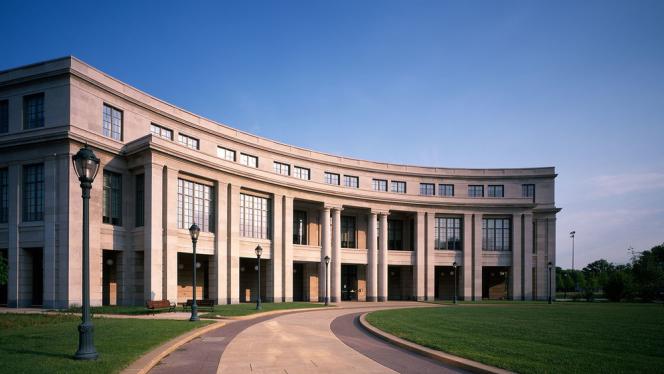 Photograph of the Kelvin Smith Library building, a large stone building with a curved facade that has columns and windows, with a grassy oval in front