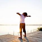 Young boy with his arms stretched wide standing on a dock in the sunlight